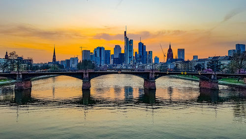 Bridge over river in city against sky during sunset