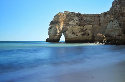 Rock formation in sea against clear blue sky