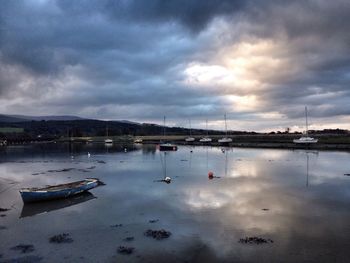 Boats moored in calm sea against cloudy sky