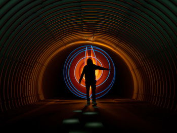 Rear view of silhouette man standing in illuminated tunnel