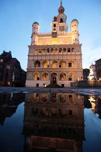 Reflection of illuminated poznan town hall in puddle against sky at twilight