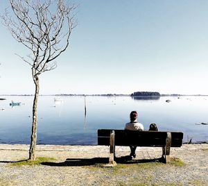 Man sitting on bench by lake against sky