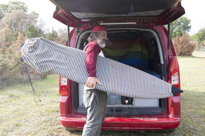 Side view of a man with a beard and a cap taking a surfboard out of the car