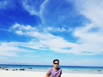 Portrait of young man wearing sunglasses at beach against sky