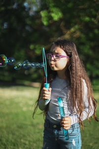 Portrait of a caucasian girl blows soap bubbles while standing in a park on a playground meadow