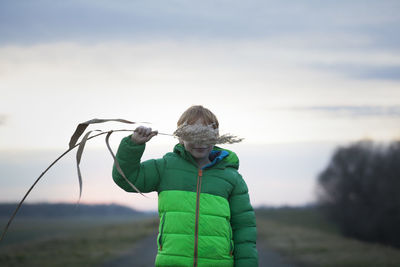 Boy holding plant while standing on road against sky during winter