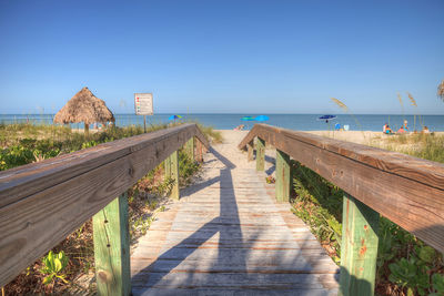 Footpath leading towards sea against clear blue sky