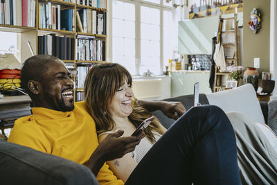 Cheerful couple sitting together with mobile phones on sofa in living room at home