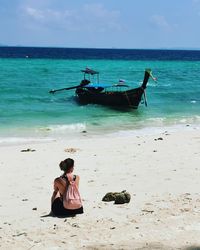 Rear view of woman sitting at beach against sky