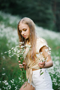 Beautiful young woman picking white wildflowers on the background of a forest landscape in summer