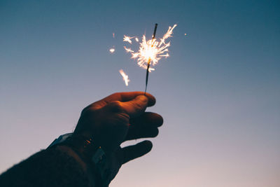 Cropped hand of man holding lit sparkler against sky