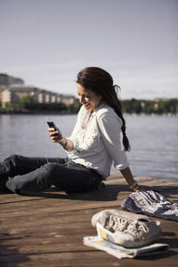 Happy businesswoman listening music while sitting on boardwalk at seaside