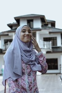 Portrait of smiling young woman standing against house