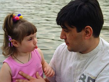 Father and daughter looking at each other against lake