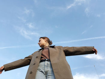 Low angle view of young woman looking away against sky