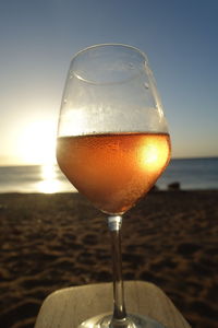 Close-up of beer in glass on beach against sky during sunset