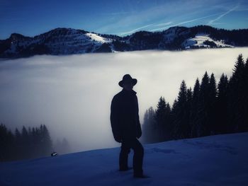 Silhouette man standing on snowcapped mountain against sky