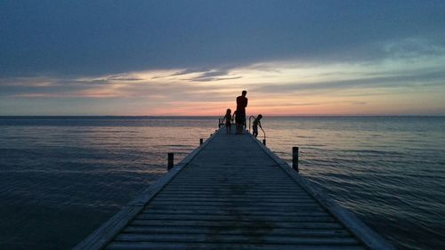 Silhouette father with children on pier over sea against cloudy sky during sunset