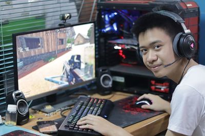 Portrait of smiling teenage boy with headphones using computer at home