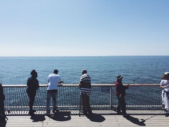 People fishing against railing by sea 