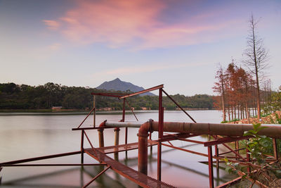 Gazebo by lake against sky during sunset