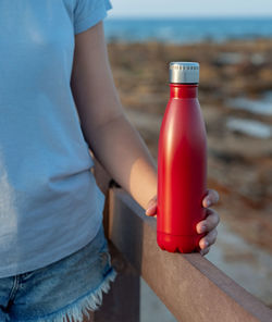 Midsection of person holding red bottle