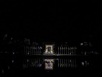 Illuminated building by lake against sky at night