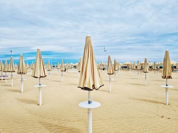 Lounge chairs and parasols on sand at beach against sky