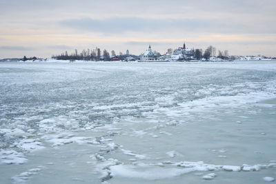 Frozen sea by buildings against sky during winter
