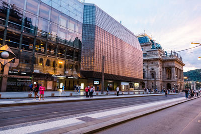 People walking on road by buildings in city