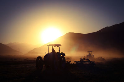 Silhouette people on field  in tractor against sky during sunrise 