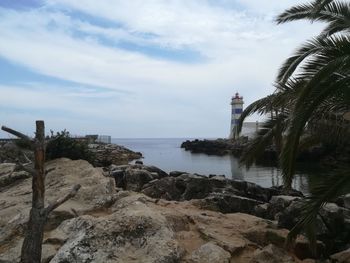 Lighthouse amidst sea and buildings against sky