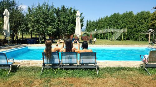 Rear view of people sitting in swimming pool against sky