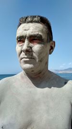 Shirtless man with mud mask standing at beach against sky