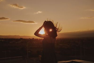 Mature woman standing on terrace against sky during sunset