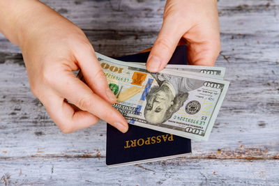 Cropped hands of woman holding passport and paper currency over table