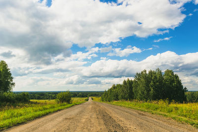 Dirt road amidst field against sky