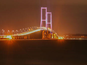 Illuminated bridge over river against sky at night