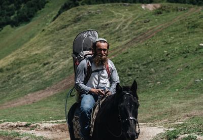 Bearded man riding horse on field during sunny day