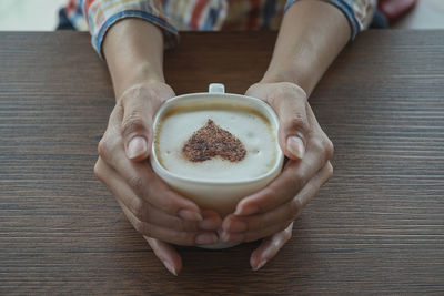 Close-up of woman holding coffee cup on table