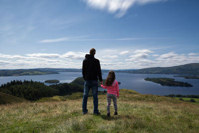 Rear view of father and daughter standing on grassy field against sky