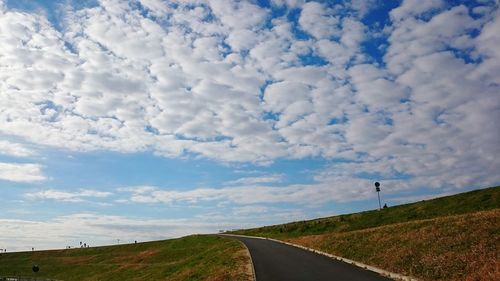 Road passing through field against cloudy sky