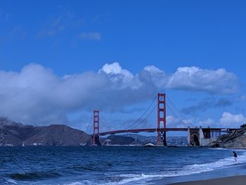 Suspension bridge over sea against cloudy sky