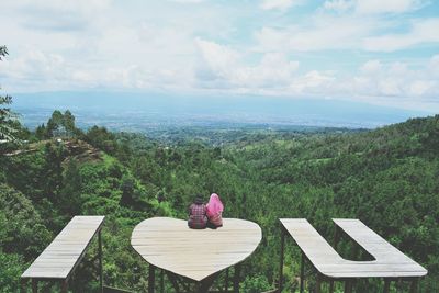 Rear view of couple sitting on i love you against sky