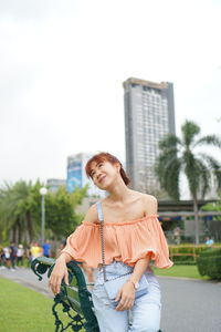 Young woman smiling while standing against sky in city