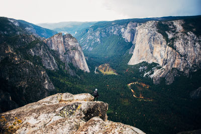 Rear view of hiker standing on cliff by rocky mountains against clear sky