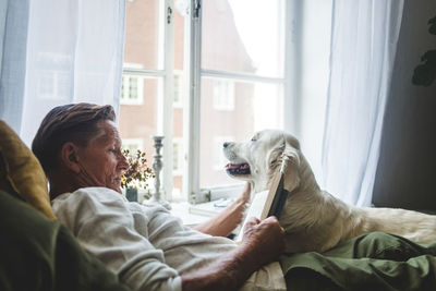 Senior man reading book while relaxing with dog on bed at home