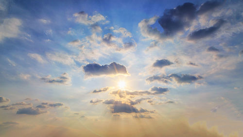 Low angle view of sunlight streaming through clouds