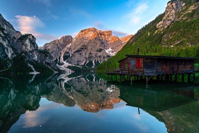 Scenic view of calm lake with stilt house and mountains reflection