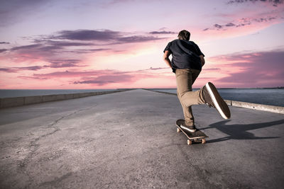 Full length of man skateboarding on road against dramatic sky